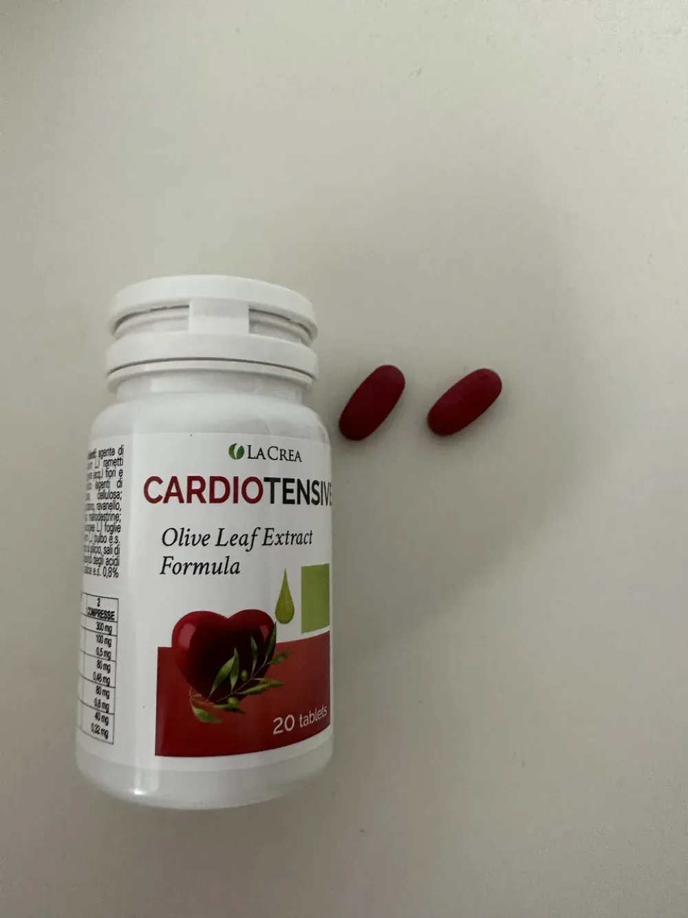 Flacone di Cardiotensive e due compresse ovali rosso-bordeaux appoggiate accanto
